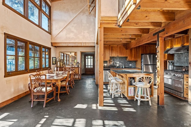 dining room featuring a towering ceiling, a healthy amount of sunlight, and beam ceiling