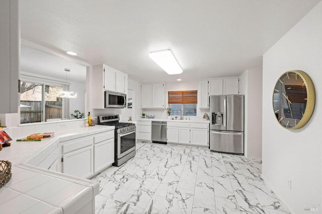 kitchen with a sink, white cabinets, marble finish floor, appliances with stainless steel finishes, and tile counters