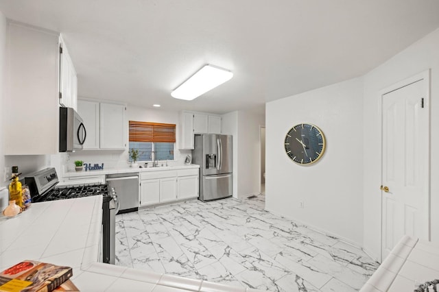 kitchen featuring tile countertops, marble finish floor, stainless steel appliances, white cabinetry, and a sink