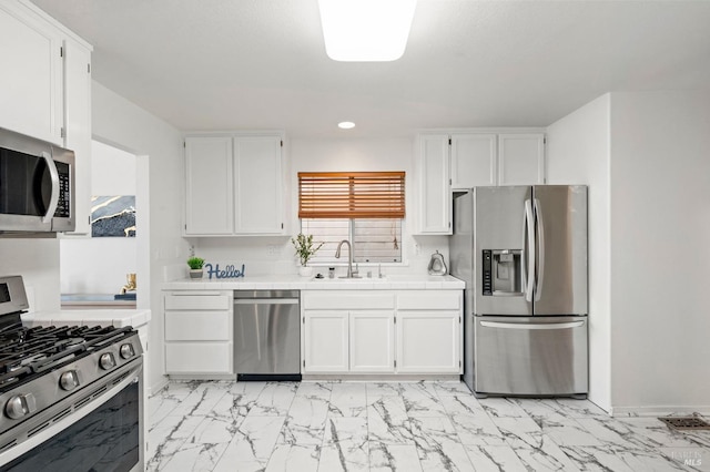 kitchen featuring appliances with stainless steel finishes, a sink, tile counters, and white cabinetry