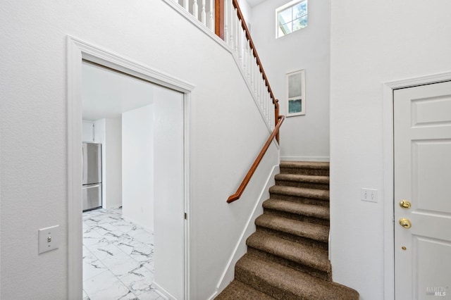 stairs featuring marble finish floor and a high ceiling