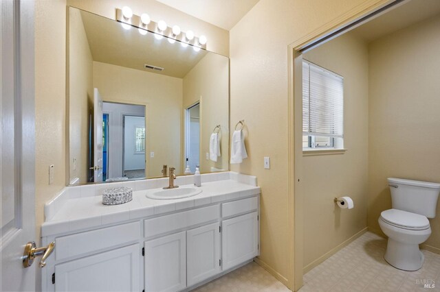 bathroom featuring toilet, vanity, baseboards, visible vents, and tile patterned floors