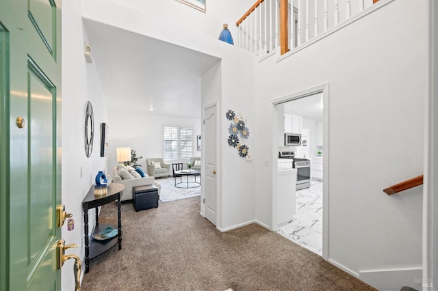 entrance foyer with carpet floors, marble finish floor, a towering ceiling, and baseboards