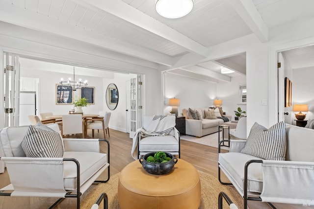 living area featuring a notable chandelier, baseboards, beam ceiling, and light wood-style floors