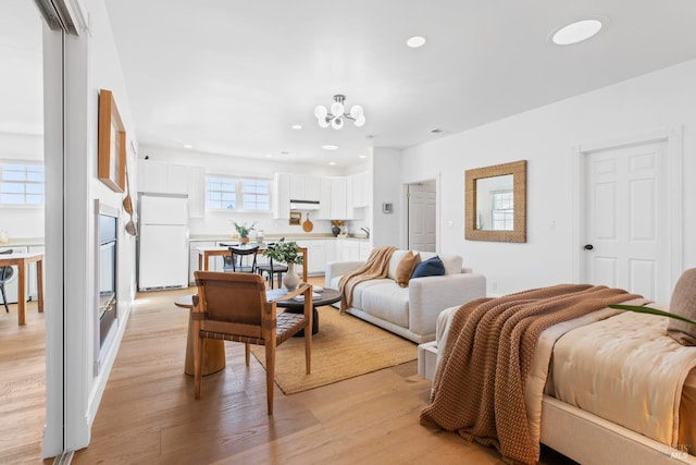 bedroom featuring light wood-style floors, freestanding refrigerator, a notable chandelier, and recessed lighting