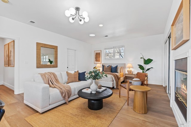 living room featuring light wood-style floors, a glass covered fireplace, visible vents, and baseboards