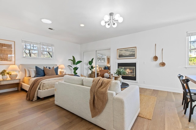 bedroom featuring a closet, visible vents, a glass covered fireplace, light wood-type flooring, and baseboards