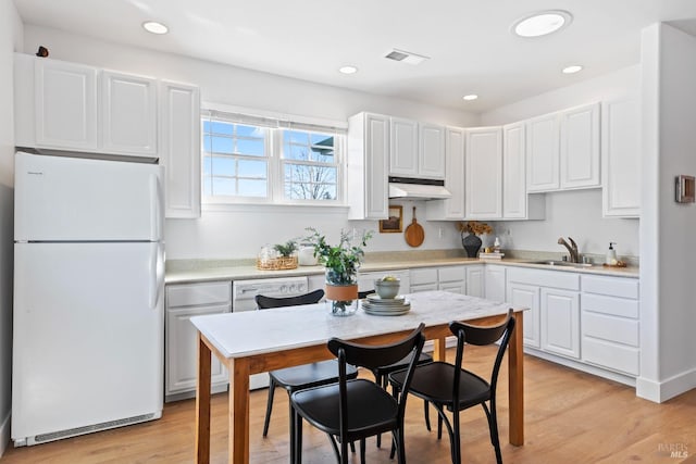 kitchen featuring under cabinet range hood, white appliances, a sink, visible vents, and light wood-type flooring