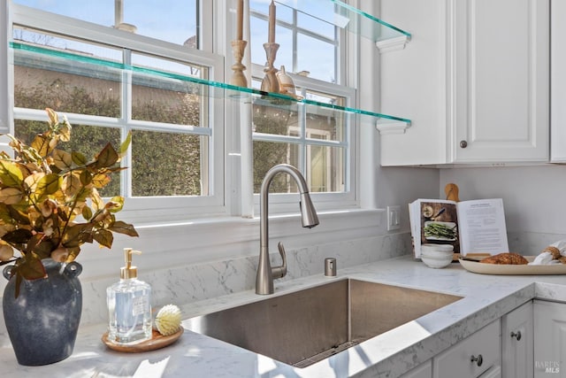 details with white cabinetry, light stone counters, and a sink