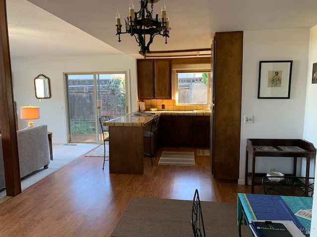 kitchen featuring dark wood-type flooring, a kitchen breakfast bar, kitchen peninsula, a notable chandelier, and backsplash