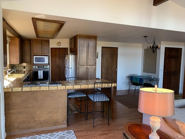 kitchen with sink, white appliances, dark hardwood / wood-style floors, tile counters, and kitchen peninsula