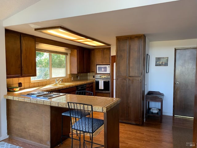 kitchen with a breakfast bar, black oven, stainless steel gas stovetop, decorative backsplash, and kitchen peninsula