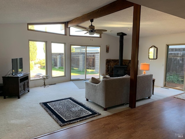 living room with lofted ceiling with beams, a textured ceiling, a wood stove, hardwood / wood-style flooring, and ceiling fan