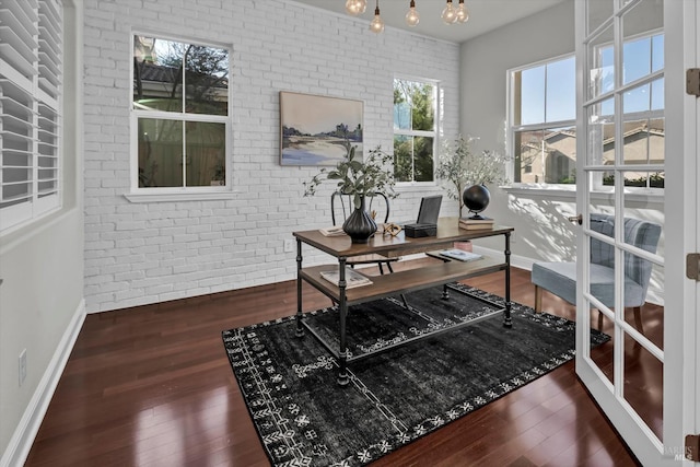 home office with brick wall and dark hardwood / wood-style flooring