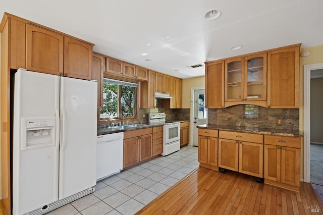 kitchen featuring decorative backsplash, under cabinet range hood, a sink, white appliances, and glass insert cabinets