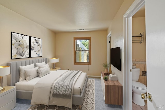 carpeted bedroom with ensuite bath, visible vents, and tile walls