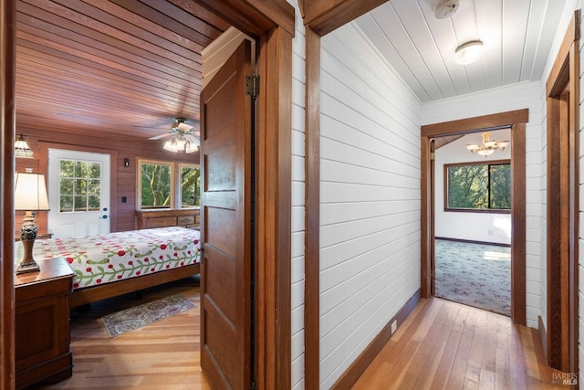 hallway with wooden walls, an inviting chandelier, wood ceiling, and light wood-type flooring