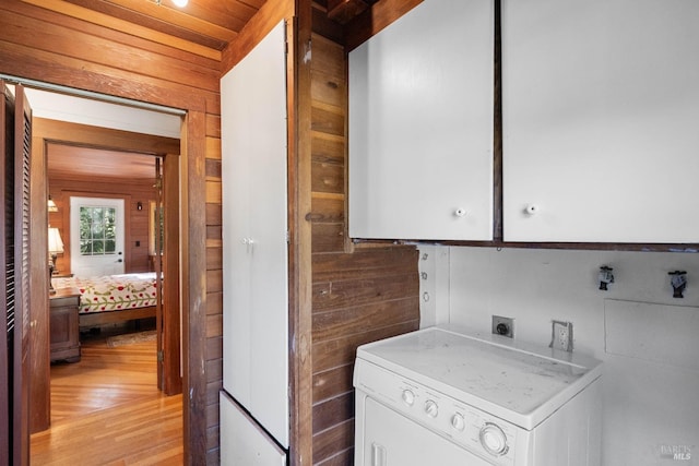 clothes washing area featuring cabinets, washer / clothes dryer, light hardwood / wood-style flooring, and wooden walls