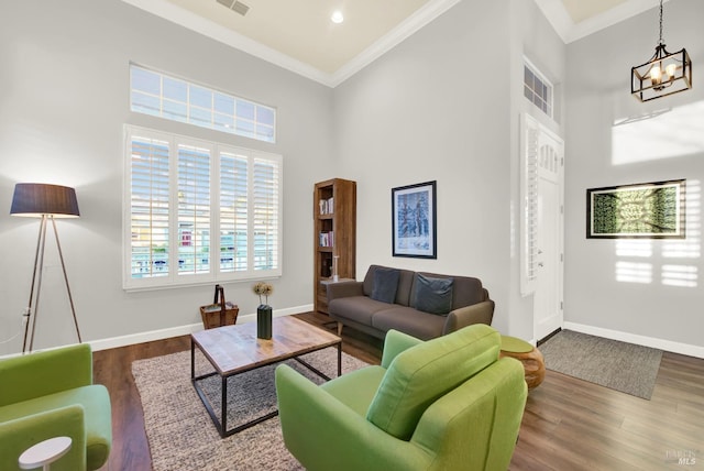 living room featuring a notable chandelier, crown molding, a towering ceiling, and hardwood / wood-style flooring