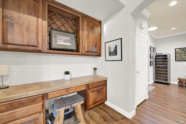 office featuring crown molding, built in desk, beverage cooler, and light hardwood / wood-style flooring