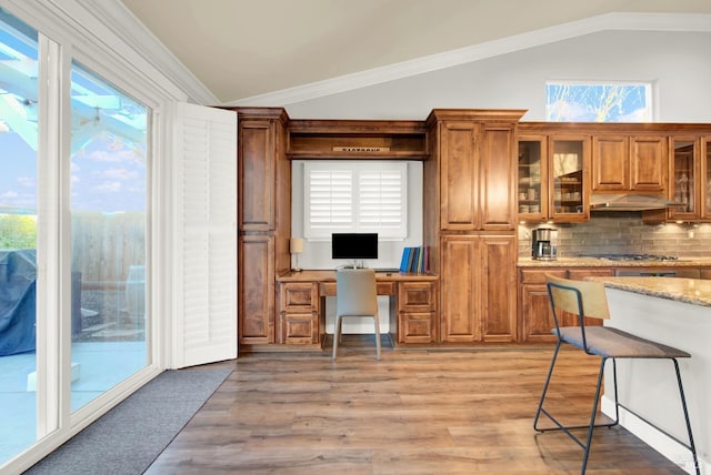 kitchen with stainless steel gas stovetop, light stone countertops, lofted ceiling, and built in desk