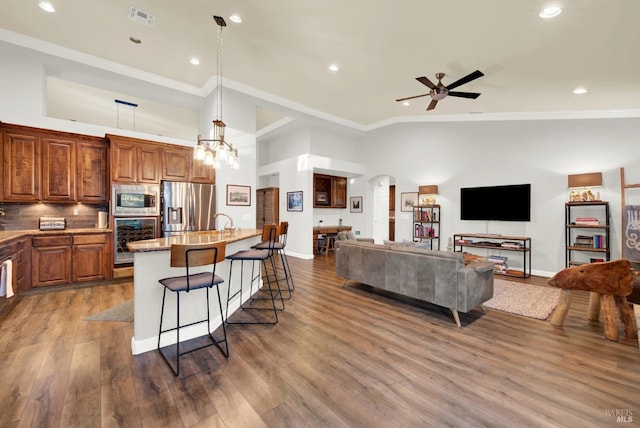 kitchen with a kitchen bar, light stone counters, hanging light fixtures, an island with sink, and stainless steel appliances