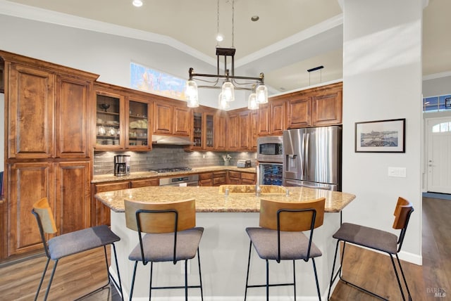 kitchen with lofted ceiling, stainless steel appliances, tasteful backsplash, light stone countertops, and a center island with sink