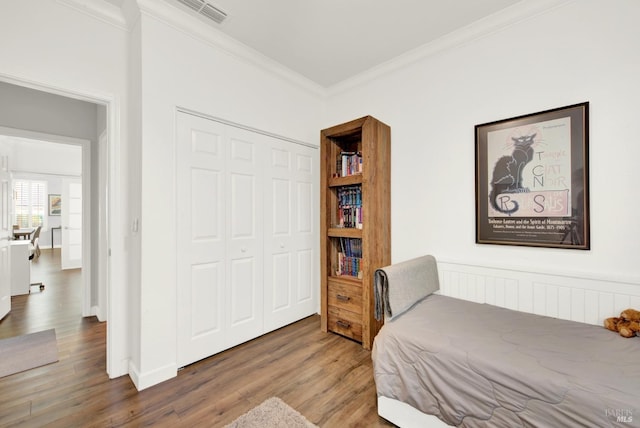 bedroom with hardwood / wood-style flooring, ornamental molding, and a closet