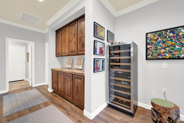 bar featuring ornamental molding, beverage cooler, and light wood-type flooring