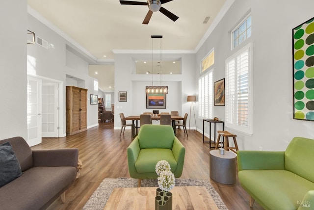 living room featuring ceiling fan, ornamental molding, wood-type flooring, and a high ceiling