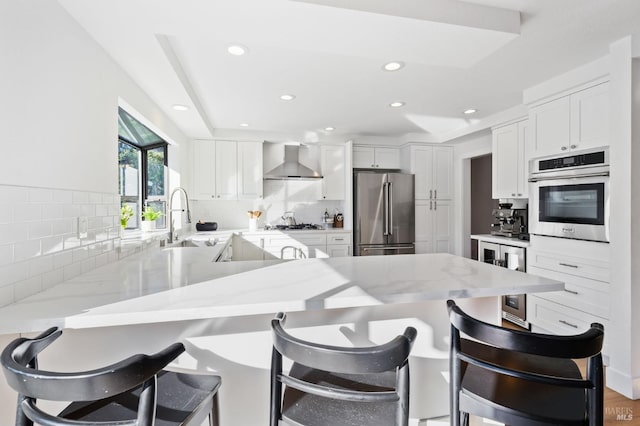 kitchen featuring wall chimney range hood, a kitchen breakfast bar, white cabinets, and appliances with stainless steel finishes