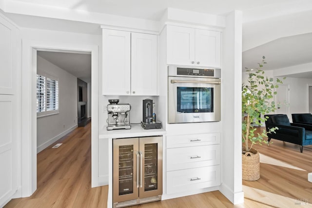 kitchen with white cabinets, light wood-type flooring, oven, and beverage cooler