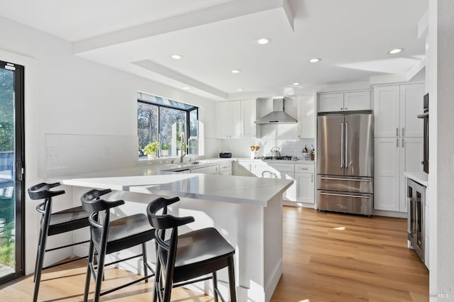 kitchen with wall chimney exhaust hood, a breakfast bar, white cabinetry, high quality fridge, and kitchen peninsula