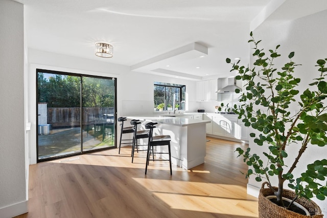 kitchen with light hardwood / wood-style flooring, a breakfast bar, white cabinetry, a kitchen island, and wall chimney exhaust hood