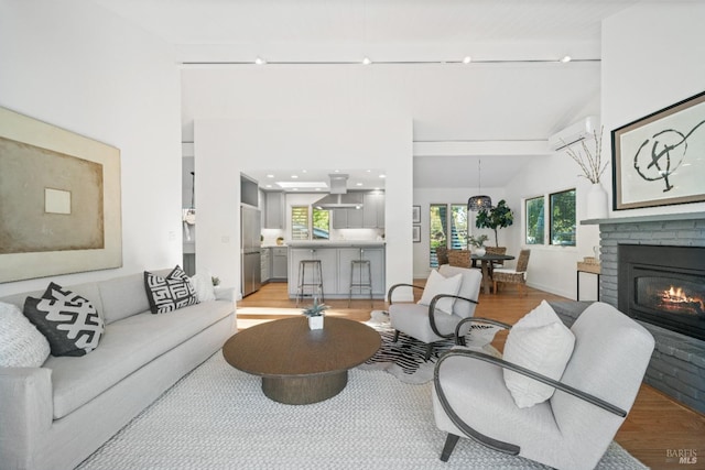 living room featuring a brick fireplace, light wood-type flooring, a wall mounted air conditioner, and lofted ceiling