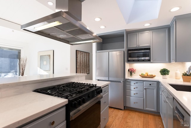 kitchen with island exhaust hood, stainless steel appliances, sink, gray cabinets, and light wood-type flooring