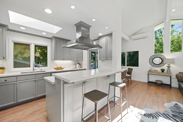 kitchen with a kitchen bar, island exhaust hood, sink, backsplash, and gray cabinetry