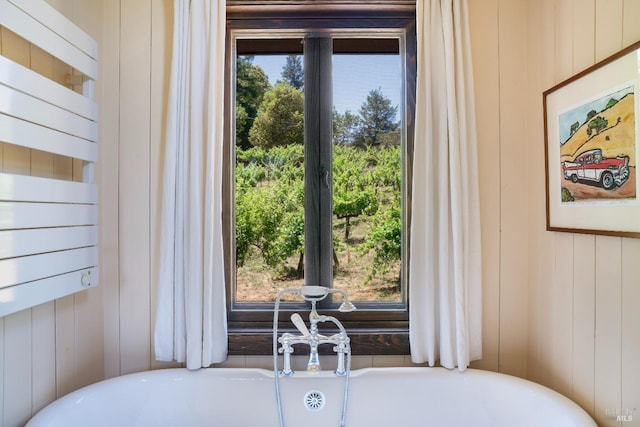 bathroom with wood walls, a tub to relax in, and a wealth of natural light