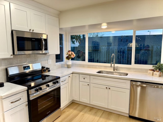 kitchen featuring sink, white cabinets, decorative backsplash, light stone counters, and stainless steel appliances