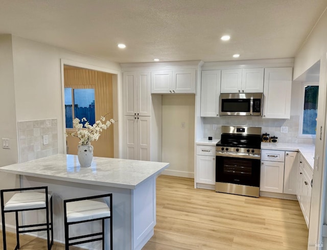 kitchen featuring white cabinetry, a kitchen bar, light stone counters, and appliances with stainless steel finishes