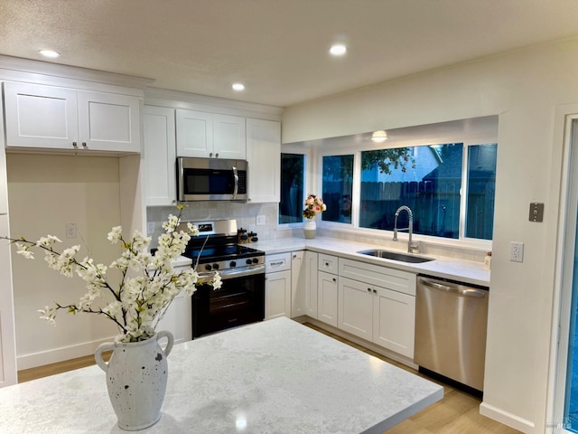 kitchen with sink, appliances with stainless steel finishes, light hardwood / wood-style floors, decorative backsplash, and white cabinets