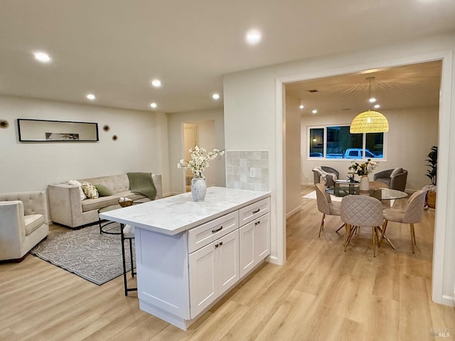 kitchen featuring a kitchen island, pendant lighting, white cabinets, light stone countertops, and light hardwood / wood-style flooring