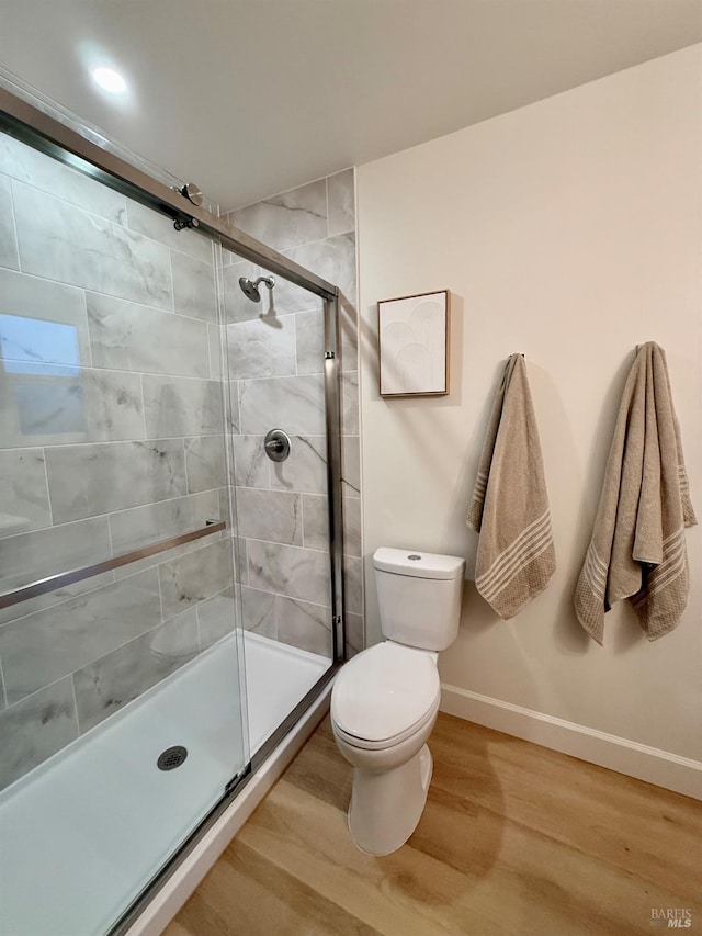 bathroom featuring toilet, a shower with door, and hardwood / wood-style floors