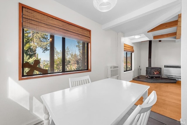 dining space featuring hardwood / wood-style floors, heating unit, beamed ceiling, a wood stove, and a wall mounted AC