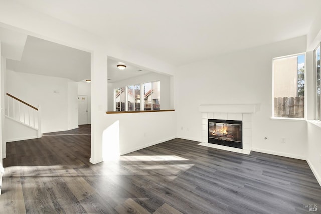 unfurnished living room featuring a wealth of natural light, a fireplace, baseboards, and dark wood finished floors
