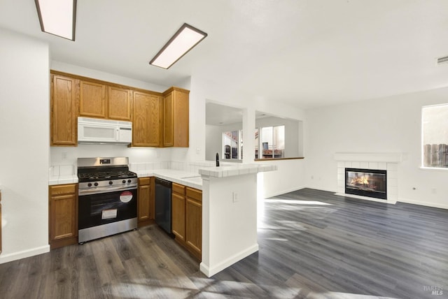 kitchen featuring white microwave, a peninsula, black dishwasher, stainless steel range with gas stovetop, and a sink