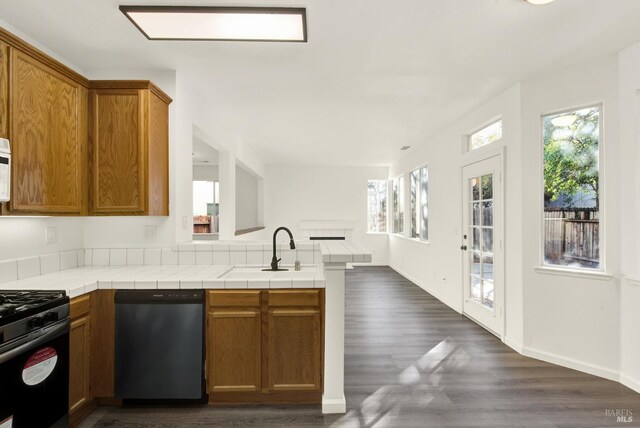 kitchen featuring stainless steel dishwasher, brown cabinetry, a peninsula, open floor plan, and gas range oven