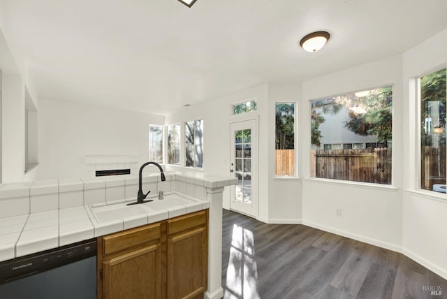 kitchen featuring tile countertops, a tiled fireplace, dark wood finished floors, dishwasher, and a sink