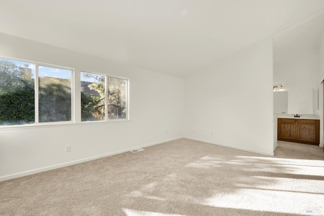 unfurnished bedroom featuring visible vents, baseboards, a sink, light carpet, and lofted ceiling