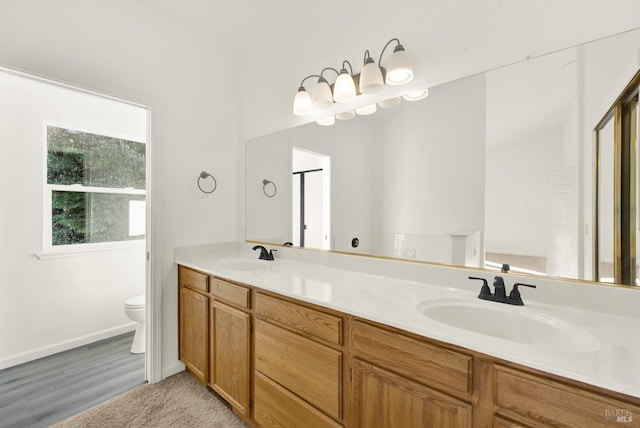 full bathroom with toilet, double vanity, a sink, and baseboards